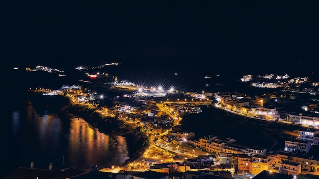 Toma aérea de edificios cerca del mar con luces encendidas durante la noche