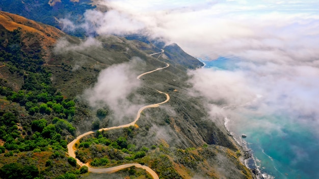 Toma aérea de hermosas colinas verdes y una carretera con curvas que bordean el increíble mar