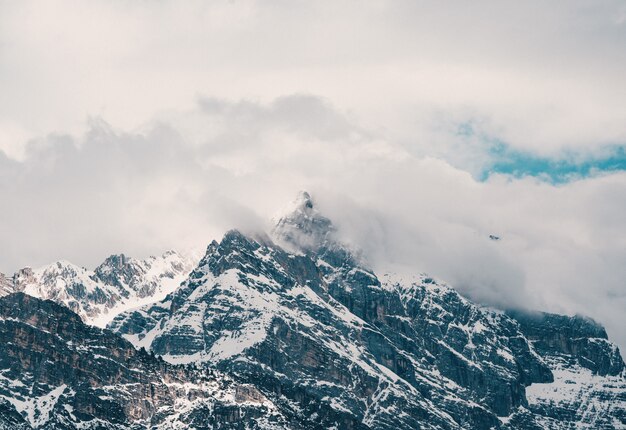 Toma aérea de hermosas montañas nevadas rocosas cubiertas de nubes
