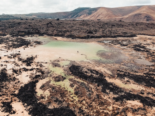 Toma aérea de un hermoso lago tarn fangoso con dos personas caminando en él