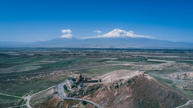 Toma aérea de una iglesia armenia en una colina con la montaña Ararat y el cielo azul claro