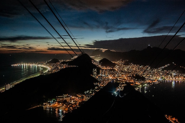 Toma aérea de las luces de los edificios de la ciudad por la noche cerca del mar y las montañas