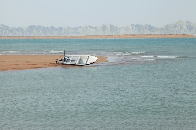 Toma aérea de un mar azul con una playa de arena y un hermoso barco blanco por el agua