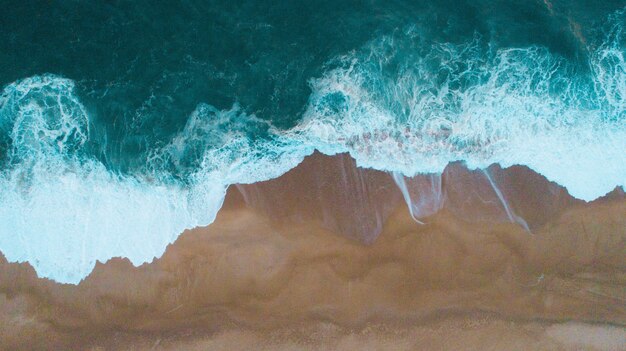 Toma aérea de las olas del mar golpeando la orilla arenosa