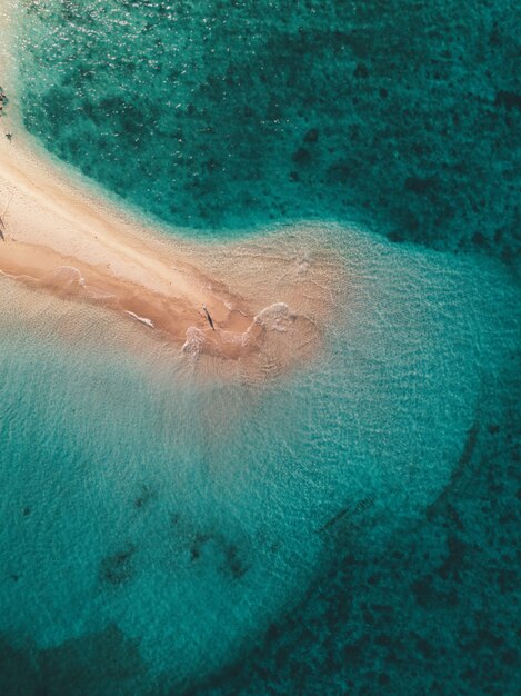 Toma aérea de las olas del mar golpeando la pequeña isla de arena