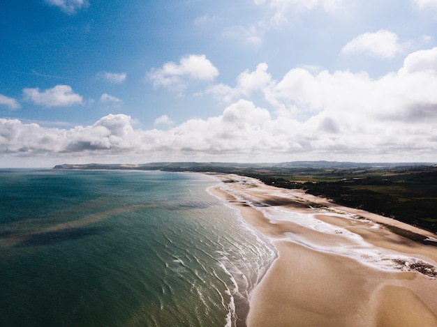 Foto gratuita toma aérea de la orilla de la hermosa playa cerca de campo de hierba con un cielo nublado