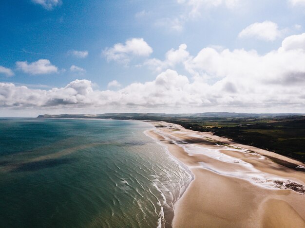 Toma aérea de la orilla de la hermosa playa cerca de campo de hierba con un cielo nublado