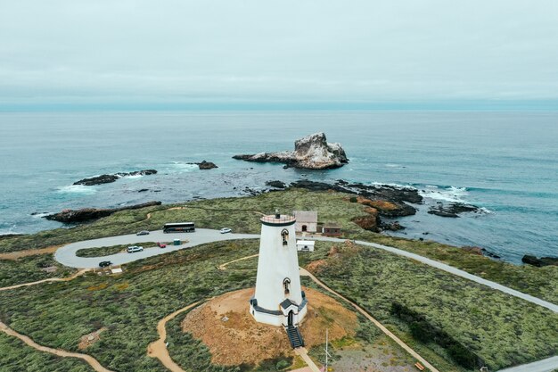 Toma aérea de una torre redonda blanca en la costa rocosa del mar