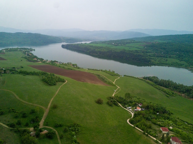 Toma aérea de los verdes paisajes, campos y un río bajo el cielo nublado en un día soleado