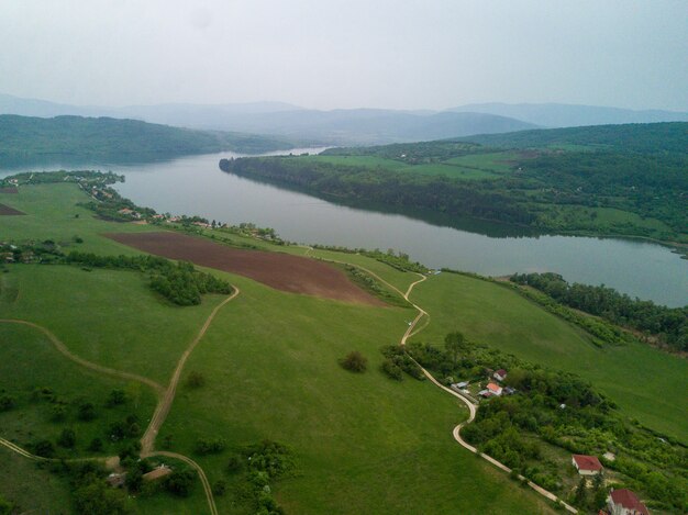 Toma aérea de los verdes paisajes, campos y un río bajo el cielo nublado en un día soleado