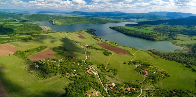 Toma aérea de los verdes paisajes, campos y un río bajo el cielo nublado en un día soleado