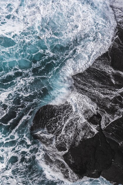 Toma aérea vertical de las olas del mar golpeando las rocas