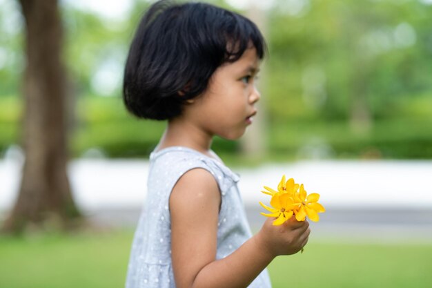 Toma de enfoque poco profunda de una niña tailandesa sosteniendo flores amarillas en el parque