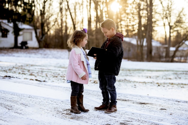 Toma de enfoque selectivo de lindos niños leyendo la Biblia en medio de un parque de invierno