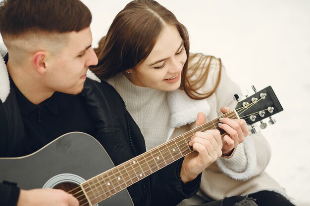 Toma de estilo de vida de pareja sentada en el bosque nevado. Personas que pasan las vacaciones de invierno al aire libre. Pareja con una guitarra.