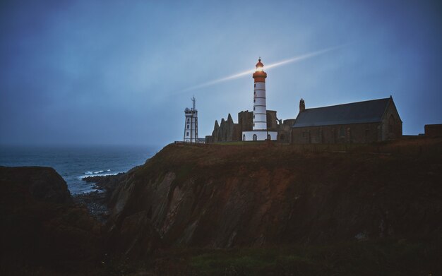 Foto gratuita toma horizontal de una ciudad misteriosa en un acantilado con un faro blanco encendido al anochecer