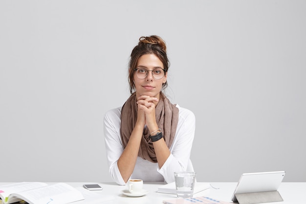 Foto gratuita toma interior de emprendedora segura de sí misma se sienta en el escritorio de la oficina, trabaja en el desarrollo de un nuevo proyecto, tiene una pausa para el café.