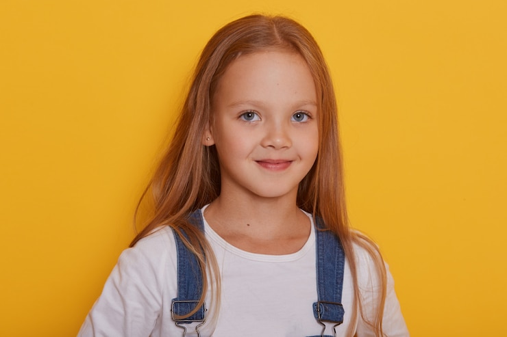 Foto gratuito toma interior de hermosa niña con cabello largo y rubio posando aislado sobre amarillo