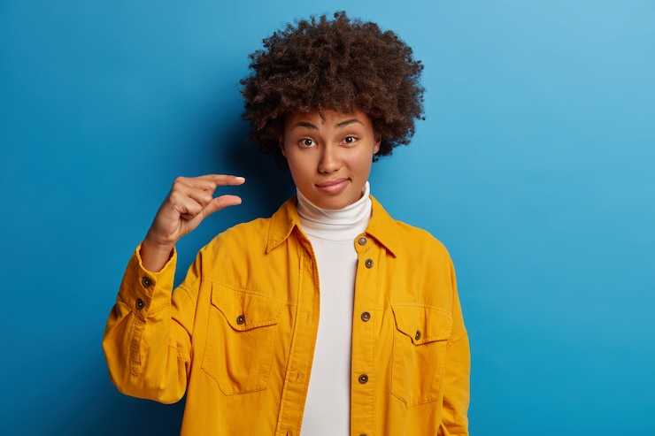 Foto gratuito la toma en interiores de una hermosa mujer de cabello rizado muestra un tamaño pequeño poco impresionante, da forma a un elemento muy pequeño, dice que es demasiado pequeño, le falta un pequeño porcentaje durante la prueba de aprobación