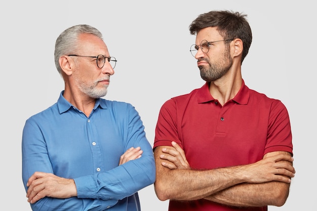 Toma en interiores de un joven disgustado que mira a su abuelo, mantiene las manos cruzadas, habla de la vida, se para uno al lado del otro, aislado sobre una pared blanca. Personas, concepto de comunicación