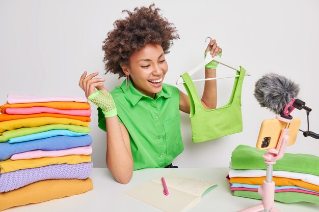 La toma en interiores de la mujer compradora en línea tiene una expresión alegre que sostiene la ropa en la percha