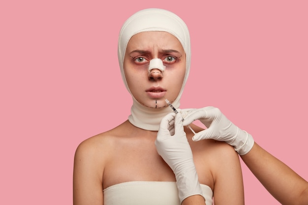Toma en interiores de una mujer joven con expresión dicontent tiene procedimiento de aumento de labios, recibe inyección de cirujano irreconocible