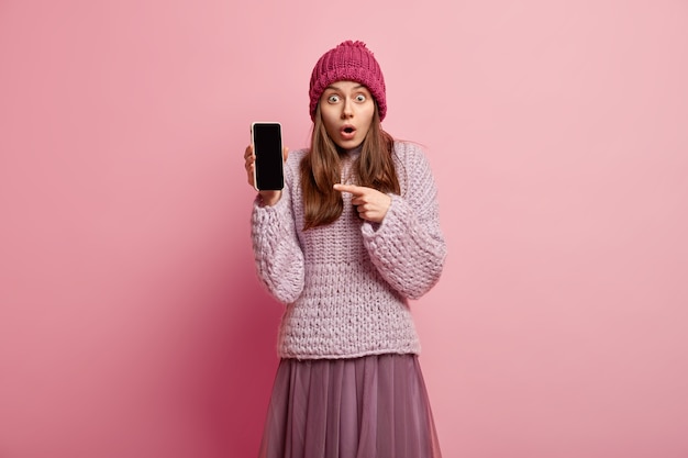 La toma en interiores de una niña milenaria sorprendida muestra la pantalla de su teléfono inteligente y promueve una aplicación de edición de fotos agradable