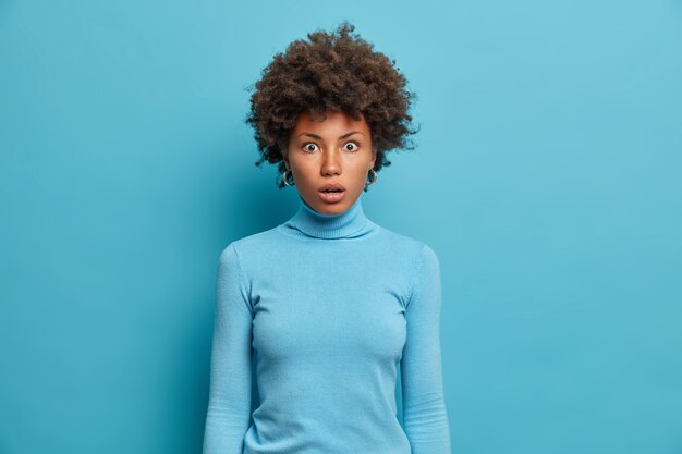 Toma de medio cuerpo de una joven afroamericana conmocionada asombrada al escuchar noticias sorprendentes, mira fijamente con ojos saltones, preocupada y frustrada, no puede creer en algo, vestida de manera informal