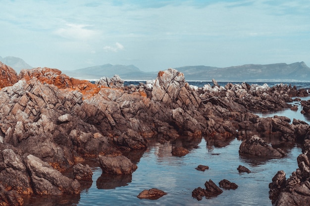 Toma de paisaje de grandes rocas en la orilla del mar con un cielo nublado y montañas