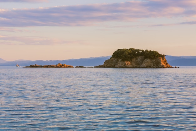 Toma panorámica de un acantilado sobre el cuerpo de un mar en calma bajo un cielo rosado