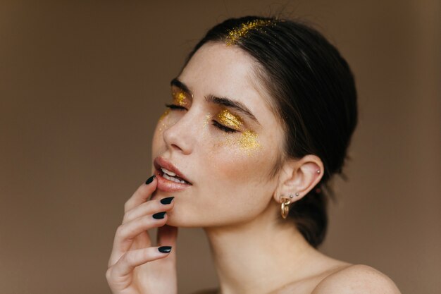 Toma de primer plano de alegre modelo femenino con cabello negro. Retrato interior de mujer caucásica despreocupada tocando sus labios.