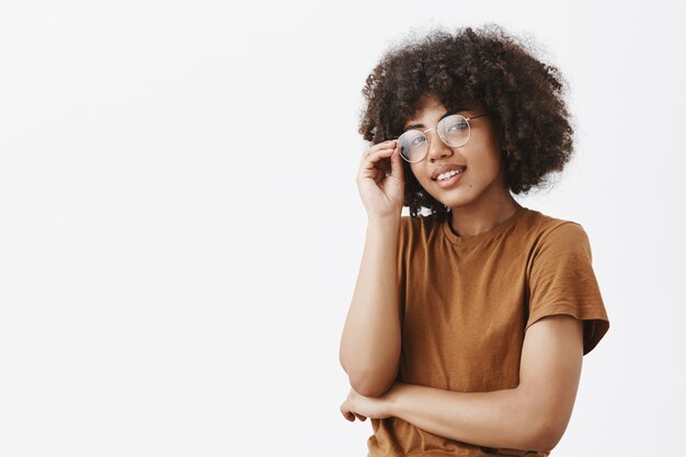 Toma de primer plano de mujer de piel oscura moderna elegante y guapa tocando gafas y mirando con expresión relajada satisfecha teniendo confianza en sí misma