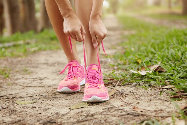 Toma recortada de corredor de mujer joven apretando los cordones de las zapatillas, preparándose para hacer ejercicio al aire libre.