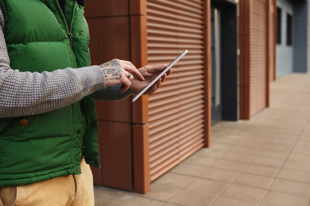 Foto gratuita toma recortada de hombre joven de moda irreconocible con mensaje de escritura de tatuaje en computadora portátil digital, chateando en línea o navegando por internet. cerca de gadget electrónico en manos del hombre