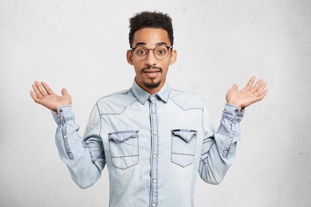 Toma recortada de moda joven hombre viste ropa de mezclilla y gafas, gestos con las manos,