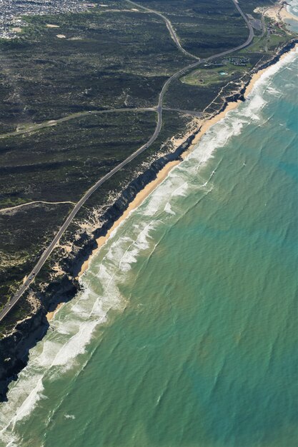 Toma vertical aérea de una carretera en medio de campos de hierba cerca de una orilla de playa