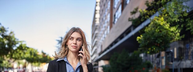 Foto gratuita toma vertical de una joven empresaria segura de sí misma haciendo una llamada telefónica parada en la calle y hablando