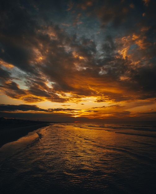 Toma vertical de una playa rodeada por las olas del mar bajo un cielo nublado durante una hermosa puesta de sol