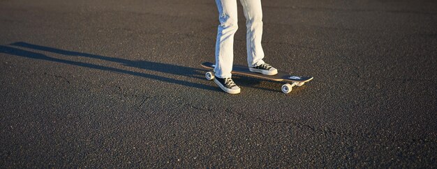 Foto gratuita tomada cortada de las piernas en una patinadora de longboard montando su patineta en la calle una adolescente femenina en