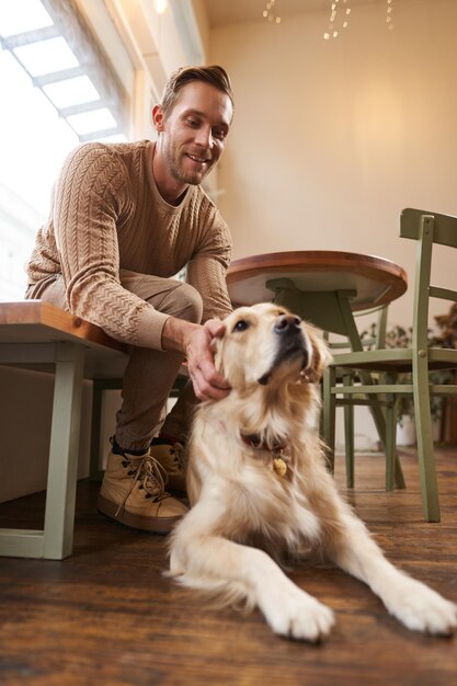 Tomada vertical de un joven sonriente con su perro golden retriever en un café