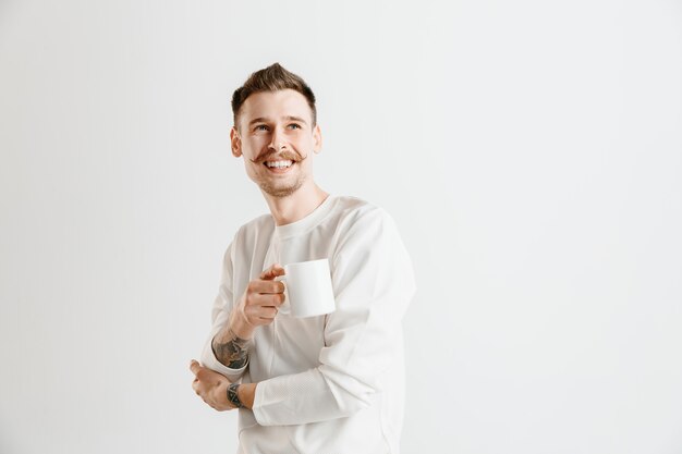 Tomando un café. Apuesto joven sosteniendo la taza de café mientras está de pie contra el fondo gris del estudio