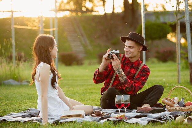 Tomando foto. Pareja joven caucásica disfrutando juntos de fin de semana en el parque el día de verano. Luce encantadora, feliz, alegre. Concepto de amor, relación, bienestar, estilo de vida. Emociones sinceras.