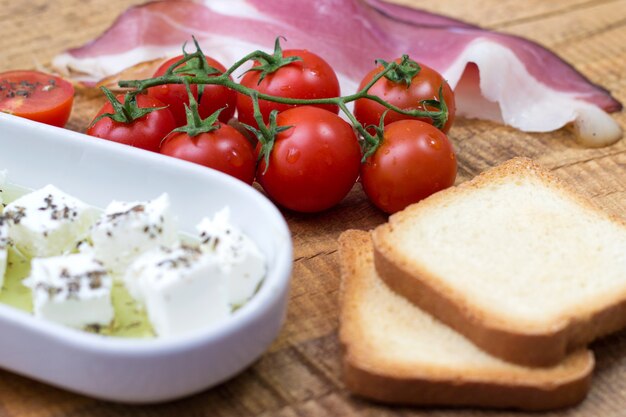 Tomate cherry, queso y prosciutto con pan tostado en la mesa de madera