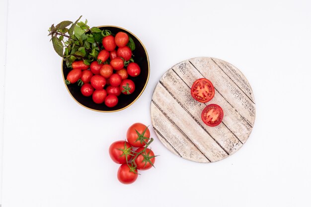 Tomate cherry y verduras en un tazón negro tomates sobre tabla de madera aislada en la superficie blanca