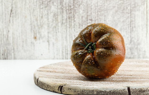 Tomate Kumato en una pieza de madera plana yacía en una pared blanca y sucia