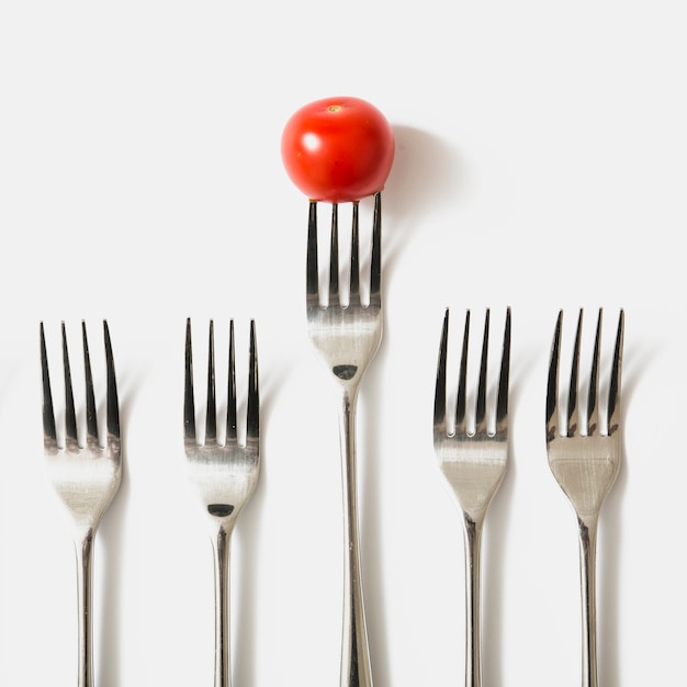 Tomate rojo cereza en tenedor contra el fondo blanco