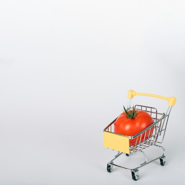 Tomate rojo fresco en carrito de compras en superficie blanca