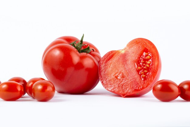 Tomate rojo fresco recogido y en rodajas junto con tomates cherry rojos en escritorio blanco