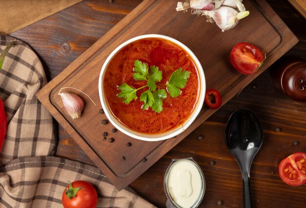 Tomate rojo, sopa de verduras borsh en un tazón de taza desechable servido con verduras verdes