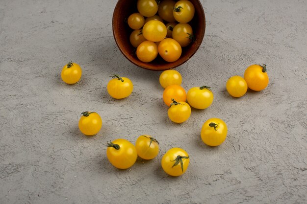 Foto gratuita tomates amarillos maduros frescos dentro y fuera de la olla redonda marrón sobre el gris